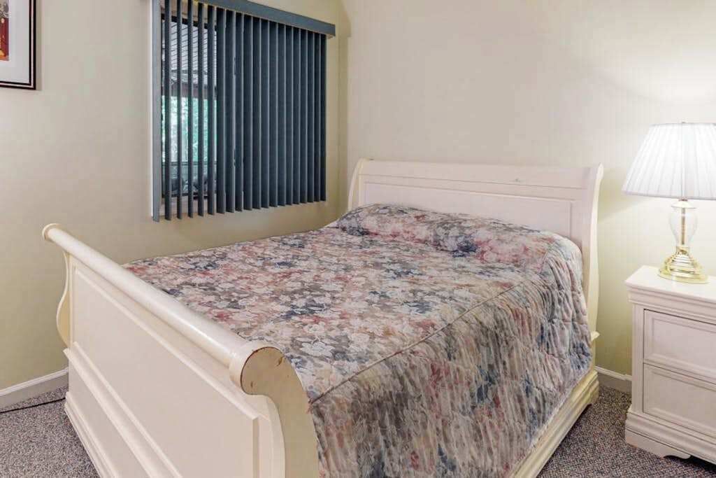 Een enkel bed met een bloemenbedekker, een nachtkastje met een lamp en een raam met zonwering.