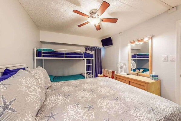 Une chambre avec un lit superposé, un ventilateur de plafond, un miroir et une commode.