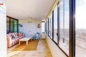 A balcony with a sofa, a chair, a table, and a view of the city. - Cozy condo in beachfront complex with pool & W/D (Ocean City)