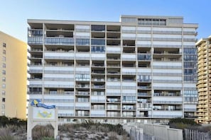 A multi-story building with balconies, a sign indicating 'High Point North,' and a sandy area in front. - Cozy condo in beachfront complex with pool & W/D (Ocean City)