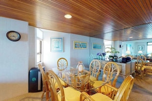 A dining area with a wooden ceiling, a round table with chairs, and framed pictures on the walls. - Cozy condo in beachfront complex with pool & W/D (Ocean City)