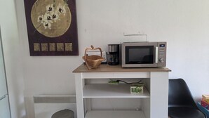 Pieni keittiönurkkaus, jossa on mikroaaltouuni, kahvinkeitin ja kori hyllyllä.