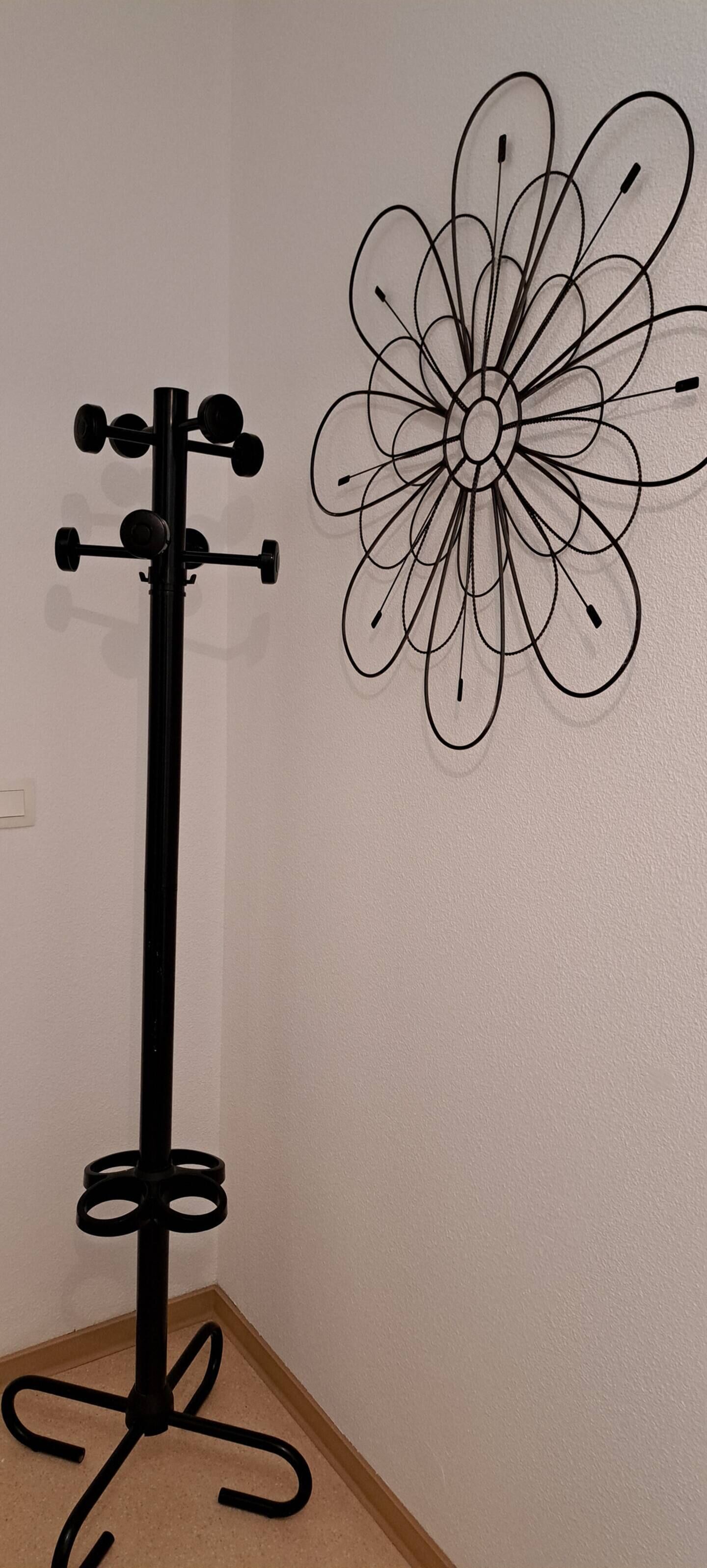 Een zwarte vloerlamp met een driepootvoet en een abstract kunstwerk aan de muur.