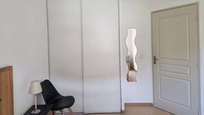 Huoneessa on liukuovellinen vaatekaappi, tuoli, lamppu ja ovi.