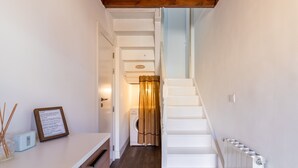 Un pasillo estrecho con una escalera que lleva a una habitación, un radiador y una pequeña mesa con un cartel enmarcado.
