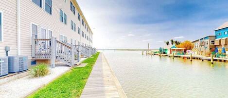 A waterfront hotel with a long dock, air conditioning units, and a grassy walkway.