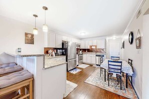 A kitchen with white cabinets, a dining area with a table and chairs, and a bench with cushions. - Bayspot L-101 (Ocean City)