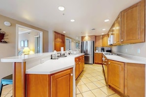 A modern kitchen with wooden cabinets, a stainless steel refrigerator, and a white countertop. - Bay & ocean views at Sea Palms - free WiFi, private washer/dryer & dog-friendly (Ocean City)
