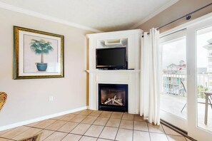 A living room with a fireplace, a television on a white entertainment unit, and a framed picture on the wall. - Bay & ocean views at Sea Palms - free WiFi, private washer/dryer & dog-friendly (Ocean City)