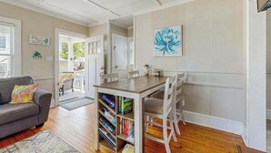 Una sala de estar con un sofá, una mesa de comedor con sillas, una estantería y una puerta que da a otra habitación.
