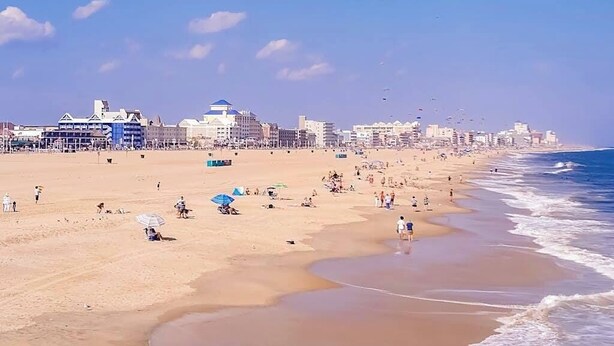 Una playa con gente, sombrillas y edificios al fondo.