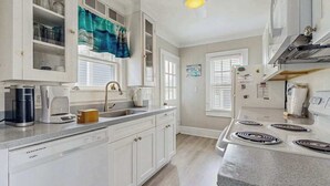 Una cocina con armarios blancos, estufa, fregadero y ventana con persianas.
