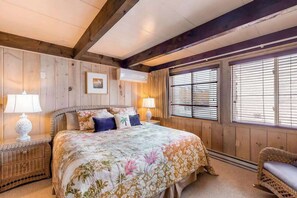 A bedroom with a large bed, wooden walls, and a window with blinds. - Oceanfront Townhome w/ Multiple Decks, Amazing Views, W/D & Beach Access (Ocean City)