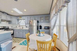 A kitchen with grey cabinets, a stainless steel refrigerator, a microwave, and a dining table with chairs. - Assateague Pointe - Bay Breeze (Berlin)