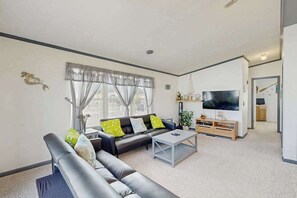 A modern living room with a sofa, coffee table, TV, and a dining area. - Assateague Pointe - Bay Breeze (Berlin)