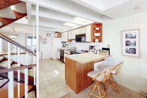 Een moderne keuken met witte kasten, een houten eiland en een eethoek met rieten stoelen.