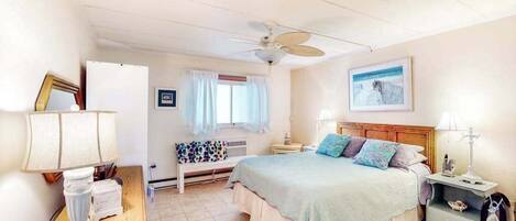 A bedroom with a bed, bedside tables, a ceiling fan, a window with curtains, a wall-mounted picture, and a floor lamp.