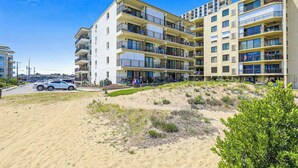 Un hotel de diversos pisos amb balcons, una platja sorrenca al davant i un cel blau i clar.