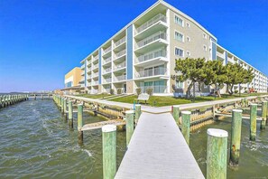 A multi-story hotel with balconies, a waterfront view, and a wooden dock leading to the water. - Thunder Island 136D (Ocean City)