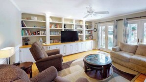 A living room with a sofa, armchair, TV, bookshelf, and a ceiling fan. - Quiet Family Home 4 Blocks from the Beach/Boardwalk with Deck, WiFi & Fireplace (Ocean City)