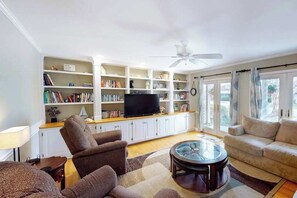 A living room with a sofa, armchair, TV, bookshelf, and a ceiling fan. - Quiet Family Home 4 Blocks from the Beach/Boardwalk with Deck, WiFi & Fireplace (Ocean City)