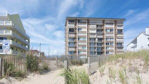 Ein mehrstöckiges Gebäude mit Balkonen, ein Sandstrand im Vordergrund und ein klarer Himmel.