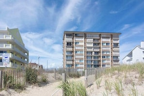 Ein mehrstöckiges Gebäude mit Balkonen, ein Sandstrand im Vordergrund und ein klarer Himmel.
