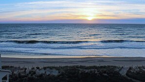 Blick auf einen Strand mit dem Meer, einem klaren Himmel und einem Sonnenuntergang.