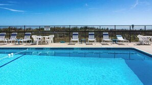 Ein Swimmingpool mit klarem, blauem Wasser, umgeben von weißen Liegestühlen und einem Zaun.