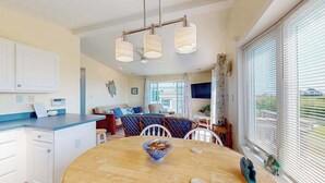 A modern kitchen with a dining area, white cabinetry, and a large window with blinds. - Assateague Pointe - Bay View Beauty (Berlin)