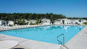 A swimming pool with lounge chairs and a table, surrounded by buildings with a view of a forested area. - Assateague Pointe - Bay View Beauty (Berlin)