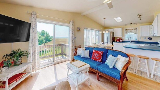 A spacious living area with a balcony, a kitchen with a bar, and a large TV. - Assateague Pointe - Bay View Beauty (Berlin)