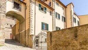 A narrow street with a building featuring a stone archway, multiple windows with shutters, and a metal gate. - Il Ponte - a romantic retreat blending history and panoramic views (Cortona)