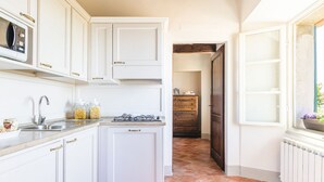 A kitchen with white cabinets, a gas stove, a microwave, and a window with a view. - Il Ponte - a romantic retreat blending history and panoramic views (Cortona)