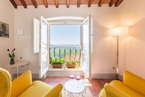 Ein Zimmer mit Balkon, zwei gelbe Sofas, ein kleiner Tisch mit zwei Weingläsern und einer Lampe.