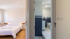 Ett hotellrum med en säng, sängbord, ett badrum med handfat och spegel samt en liten balkong.