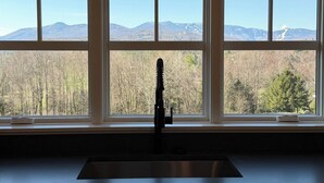 A kitchen with a stainless steel sink and a window overlooking a mountainous landscape. - Cozy 1-bedroom apartment in Stowe with amazing views, AC & gas fireplace (Stowe)