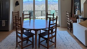 A dining area with a table and chairs, a ceiling fan, and a view through large windows. - Cozy 1-bedroom apartment in Stowe with amazing views, AC & gas fireplace (Stowe)