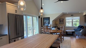 A modern kitchen with a large island, a dining area with a wooden table and chairs, a ceiling fan, and large windows. - Cozy 1-bedroom apartment in Stowe with amazing views, AC & gas fireplace (Stowe)