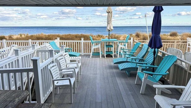 Eine überdachte Terrasse mit Stühlen und Tischen mit Blick auf den Strand.