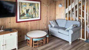 Ein Wohnzimmer mit einer Holzwand, einem gerahmten Gemälde, einem grauen Sofa, einem runden Tisch und einem Fernseher.
