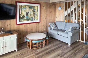 Ein Wohnzimmer mit einer Holzwand, einem gerahmten Gemälde, einem grauen Sofa, einem runden Tisch und einem Fernseher.