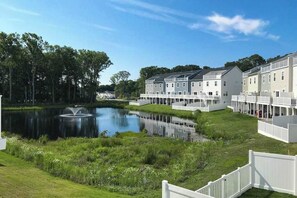 A residential area with a pond, white houses, and a clear sky.