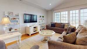 A living room with a sofa, TV, white shelving, and a large window. - Beach Retreat A (Ocean City)