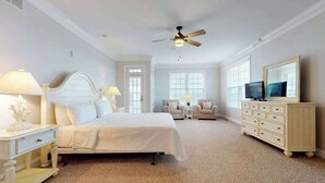 A bedroom with a bed, a ceiling fan, a TV, a dresser, and two chairs. - Beach Retreat A (Ocean City)