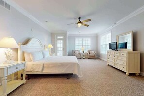 A bedroom with a bed, a ceiling fan, a TV, a dresser, and two chairs. - Beach Retreat A (Ocean City)