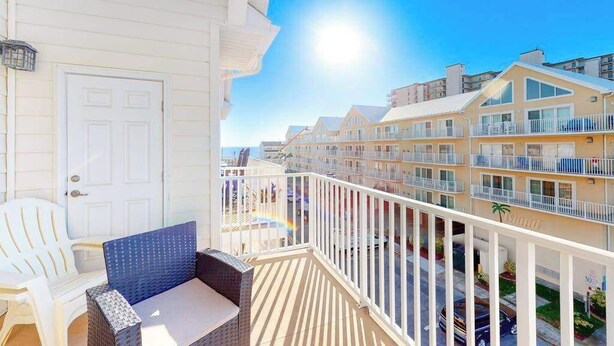 A balcony with white railings, a door, and a wicker chair. - Beach Retreat A (Ocean City)