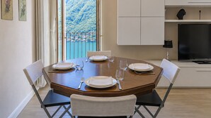 A dining area with a table set for four, a TV, and a view of a mountainous landscape. - Angela Lake View Apartment (Pognana Lario)