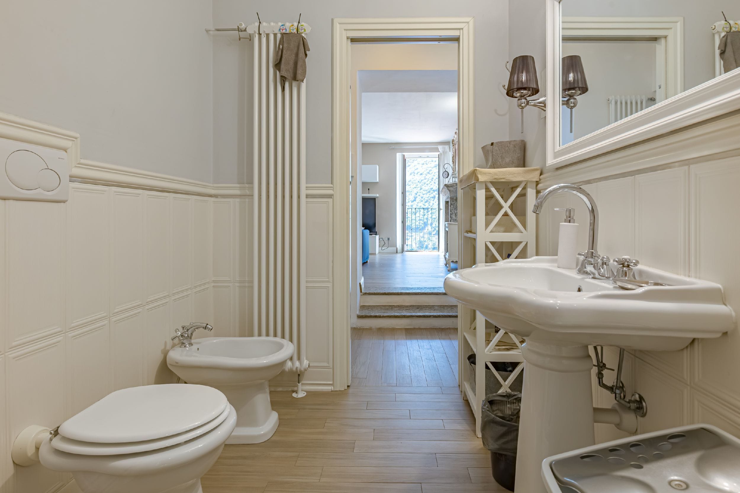 A bathroom with a toilet, bidet, sink, mirror, and towel rack.