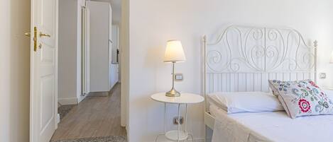 Un dormitorio con una cama, una mesita de noche con lámpara y una puerta que da a otra habitación.